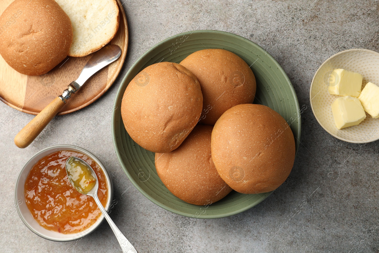 Photo of Fresh tasty buns, jam and butter on grey table, top view