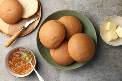 Photo of Fresh tasty buns, jam and butter on grey table, top view