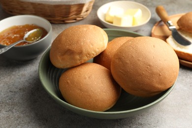 Photo of Fresh tasty buns, jam and butter on grey table, closeup