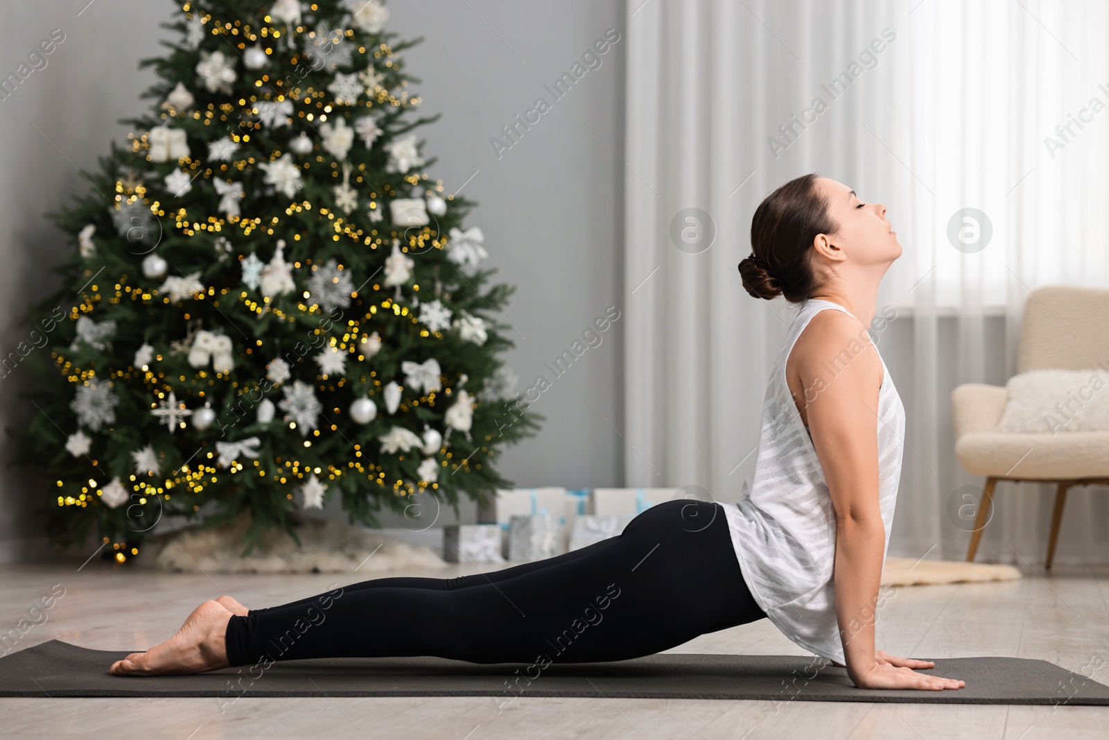 Photo of Woman practicing yoga against Christmas tree indoors