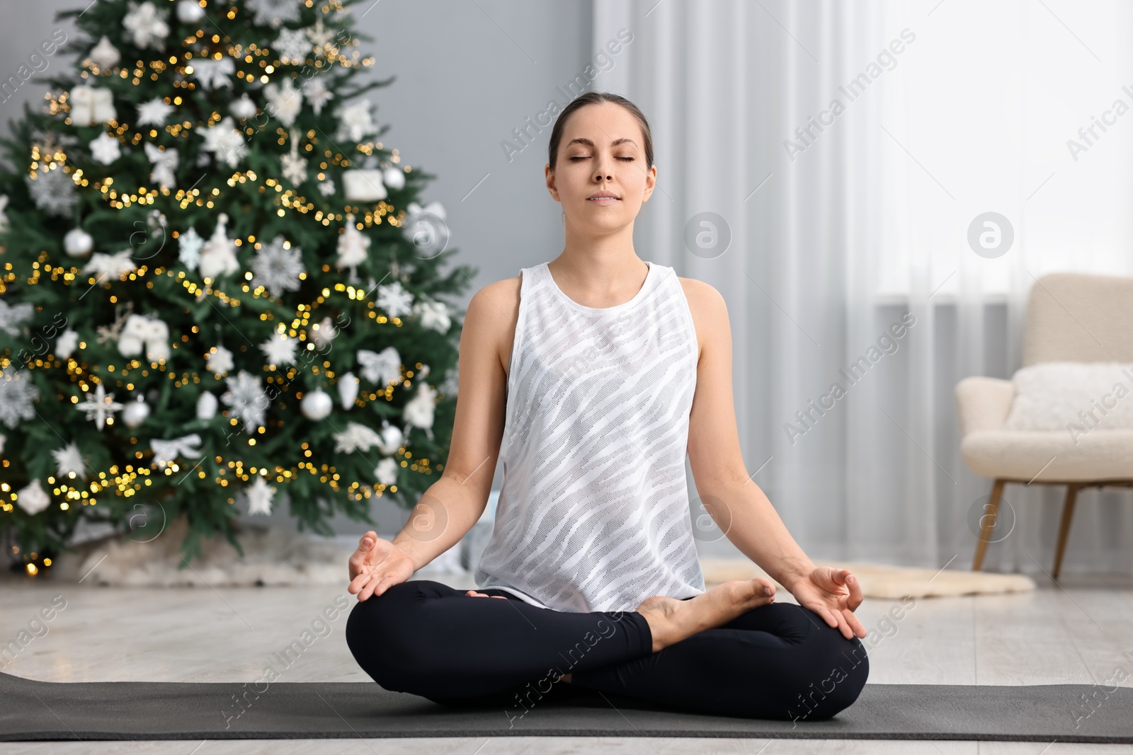 Photo of Woman practicing yoga against Christmas tree indoors