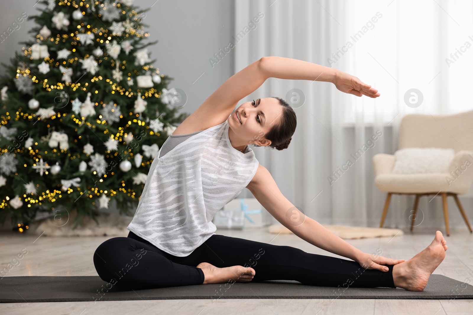 Photo of Woman practicing yoga against Christmas tree indoors