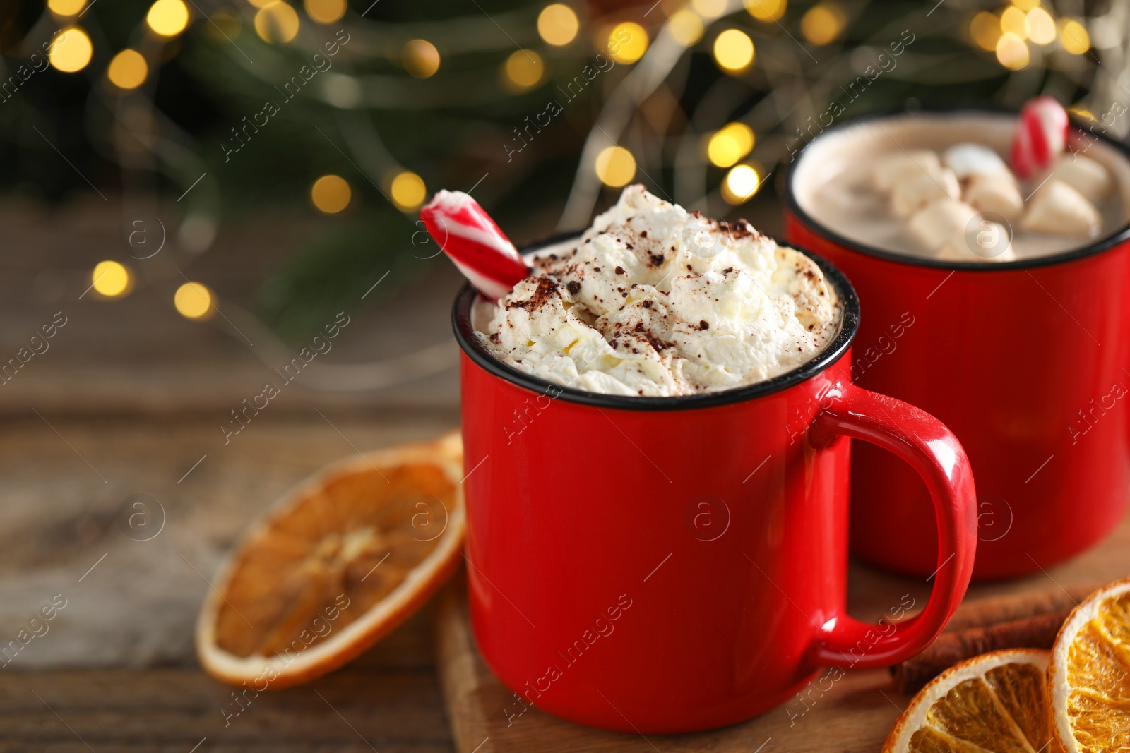 Photo of Tasty hot cocoa drink with whipped cream, marshmallows and candy canes in red mugs on table, closeup