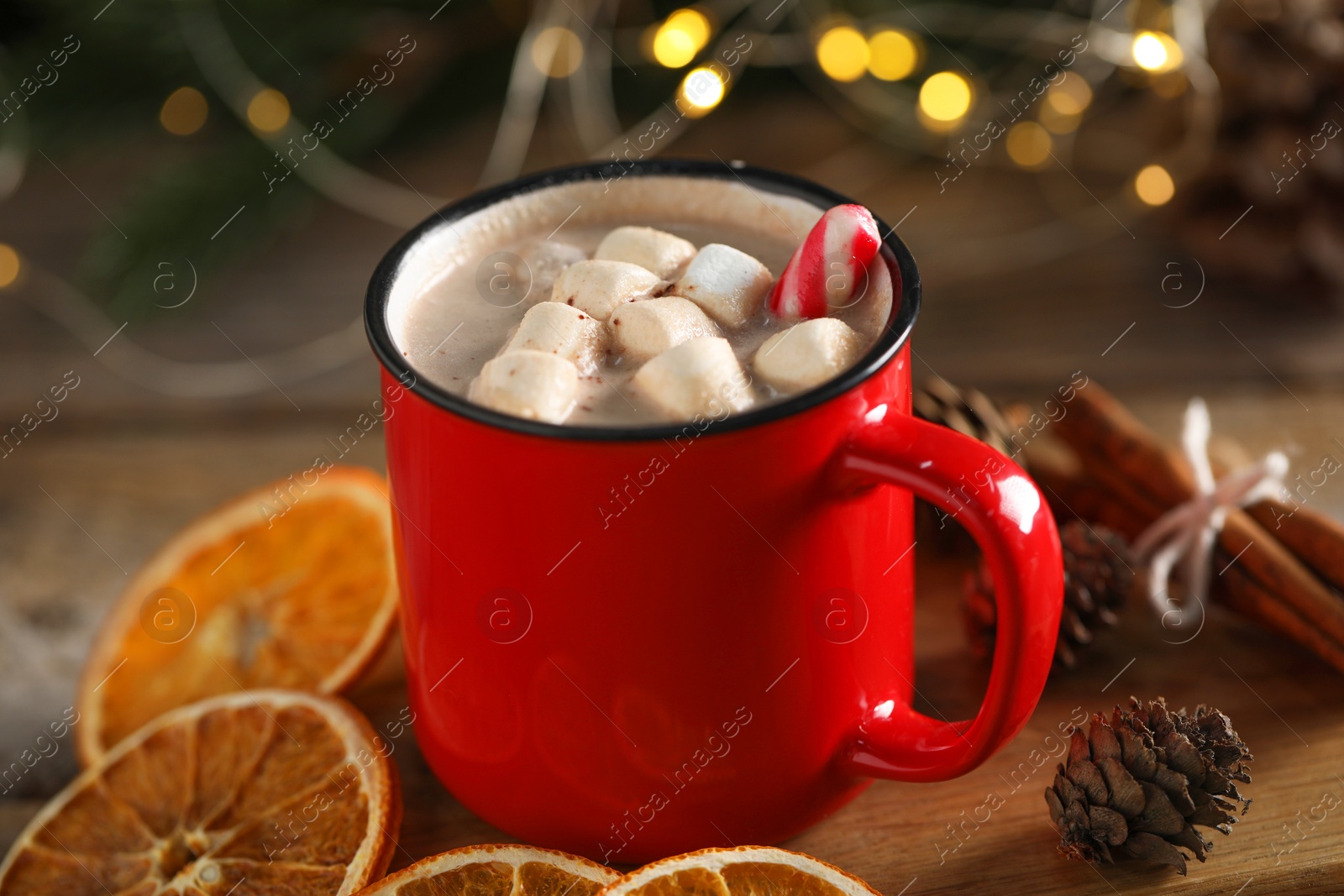 Photo of Tasty hot cocoa drink with marshmallows in red mug and spices on table, closeup