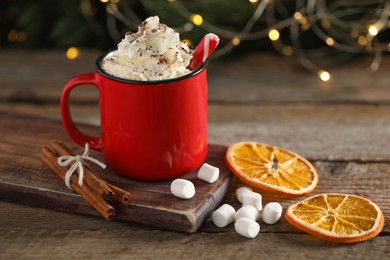 Photo of Tasty hot cocoa drink with whipped cream in mug, marshmallows and spices on wooden table