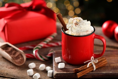 Photo of Tasty hot cocoa drink with whipped cream in mug, marshmallows and spices on wooden table