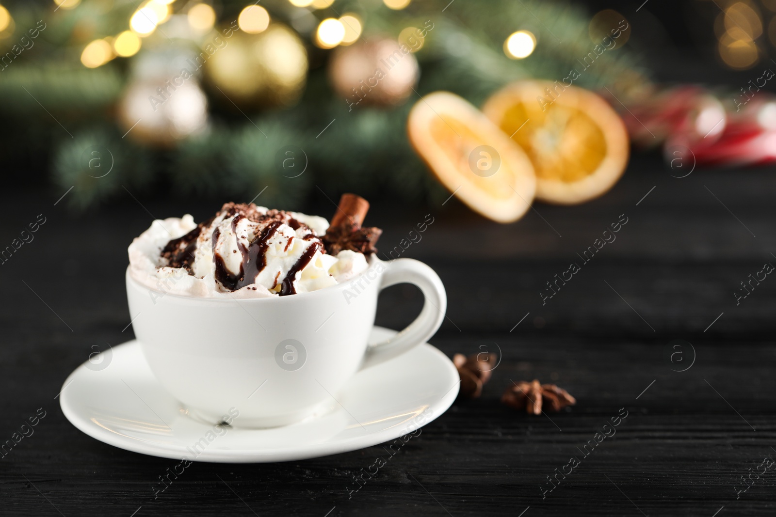 Photo of Tasty hot cocoa drink with whipped cream in cup and spices on black wooden table, space for text