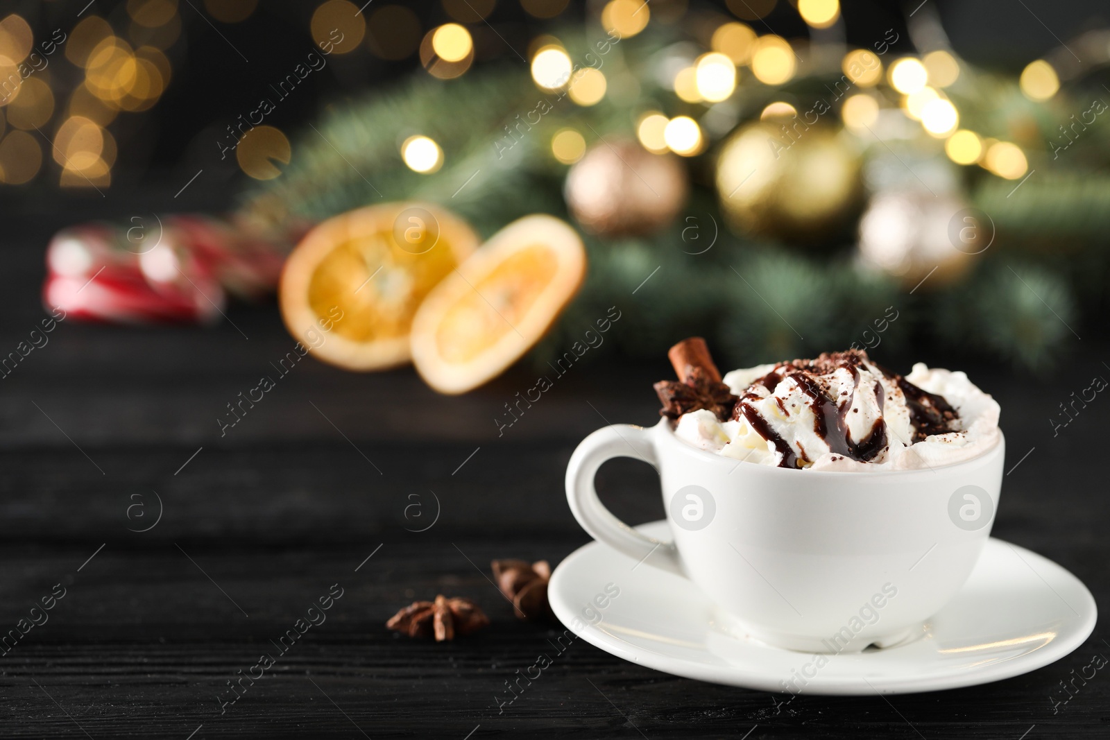 Photo of Tasty hot cocoa drink with whipped cream in cup and spices on black wooden table, space for text