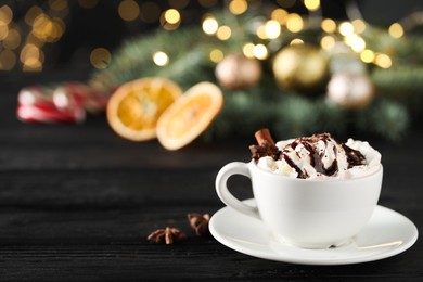 Photo of Tasty hot cocoa drink with whipped cream in cup and spices on black wooden table, space for text