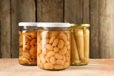 Different pickled products in jars on beige textured table