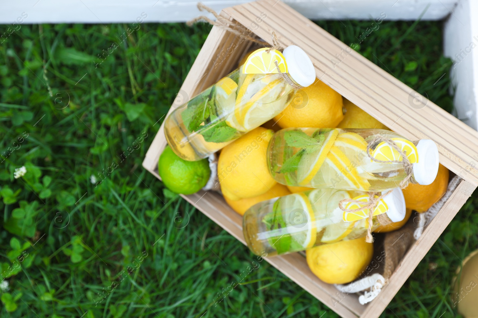 Photo of Refreshing lemonade with mint and fresh fruits in wooden crate on green grass outdoors, above view