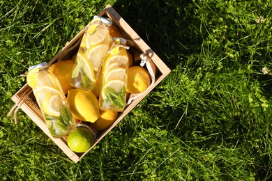 Photo of Refreshing lemonade with mint and fresh fruits in wooden crate on green grass outdoors, top view. Space for text