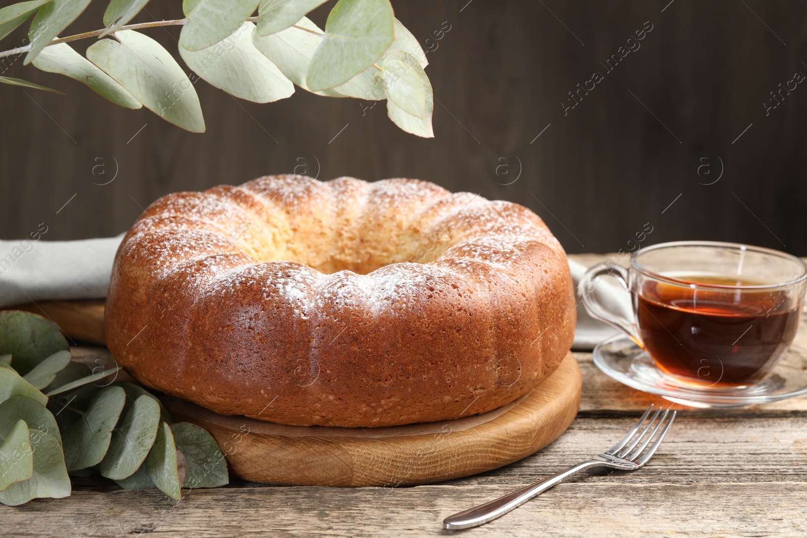 Photo of Freshly baked sponge cake, tea and eucalyptus leaves on wooden table