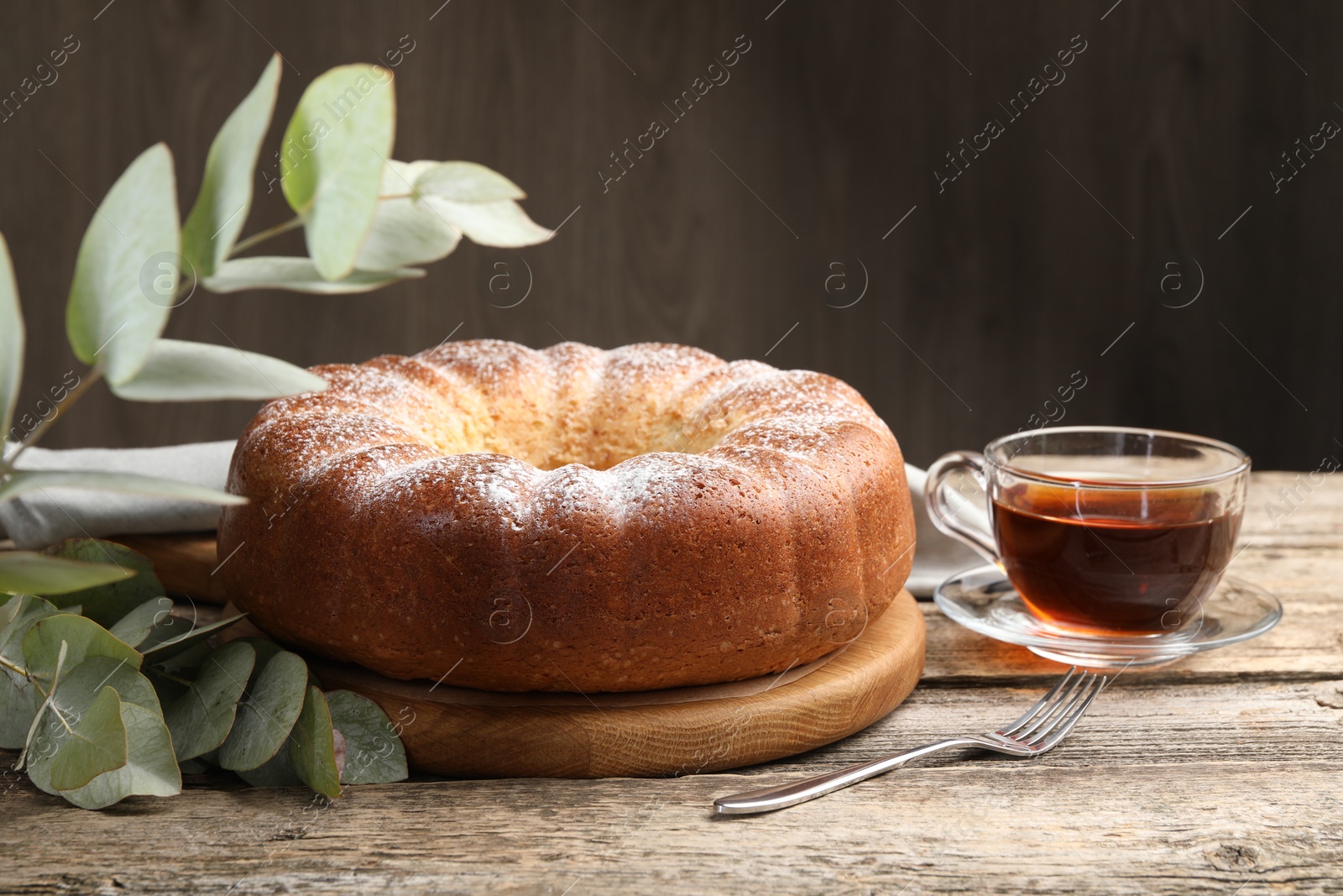 Photo of Freshly baked sponge cake, tea and eucalyptus leaves on wooden table