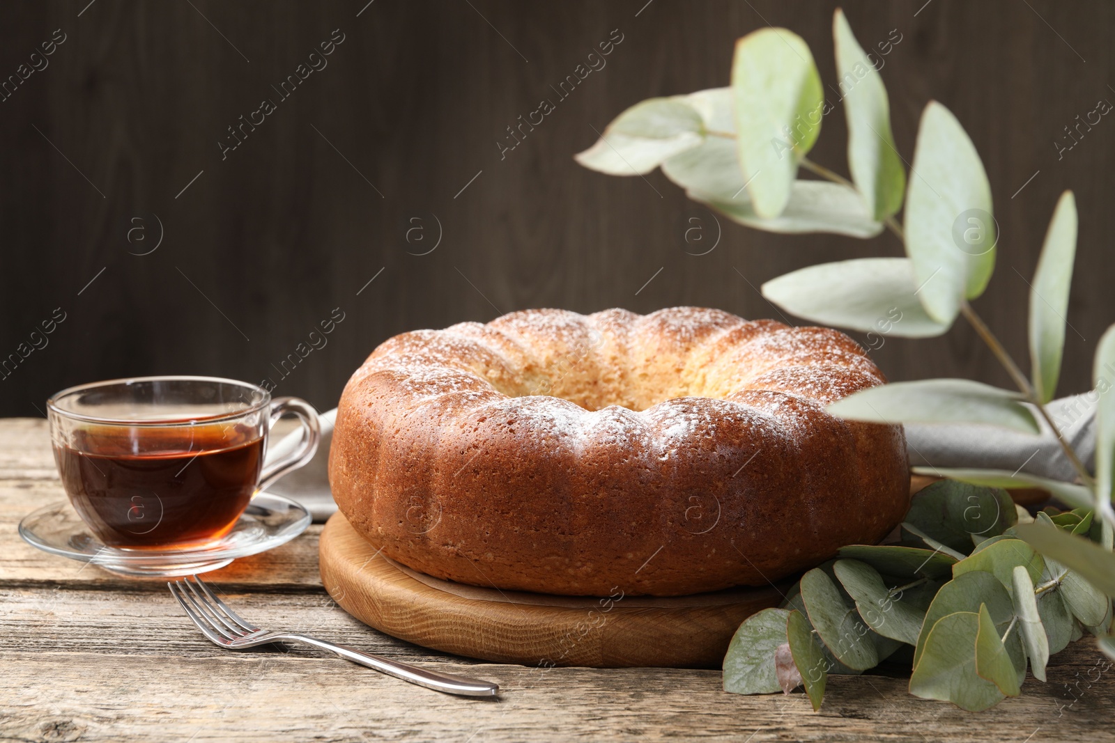 Photo of Freshly baked sponge cake, tea and eucalyptus leaves on wooden table