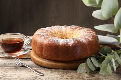 Photo of Freshly baked sponge cake, tea and eucalyptus leaves on wooden table