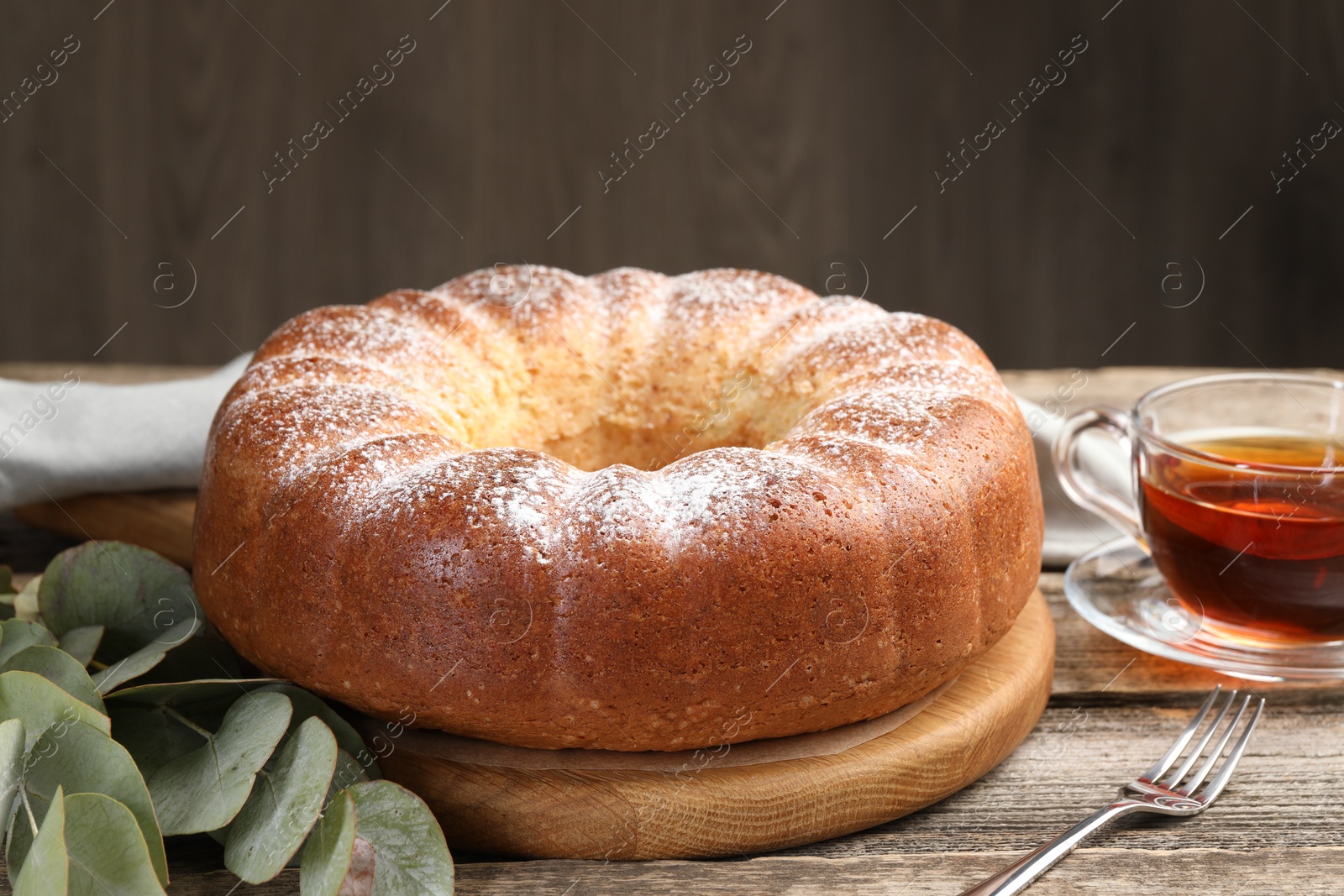 Photo of Freshly baked sponge cake, tea and eucalyptus leaves on wooden table, closeup