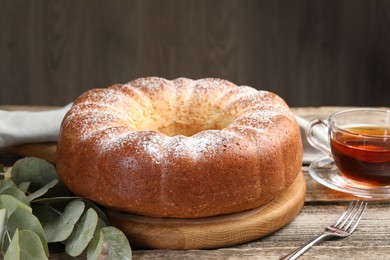 Freshly baked sponge cake, tea and eucalyptus leaves on wooden table, closeup