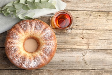 Photo of Freshly baked sponge cake, tea and eucalyptus on wooden table, top view. Space for text