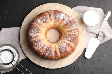 Photo of Freshly baked sponge cake with powdered sugar, milk and server on black table, top view