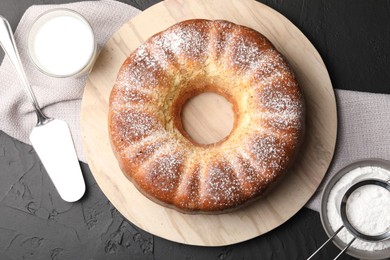 Photo of Freshly baked sponge cake with powdered sugar, milk and server on black table, top view