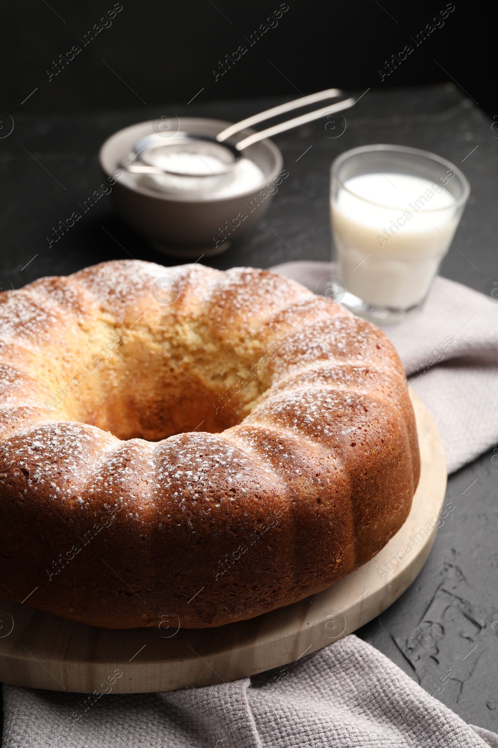 Photo of Freshly baked sponge cake with powdered sugar and milk on black table, closeup