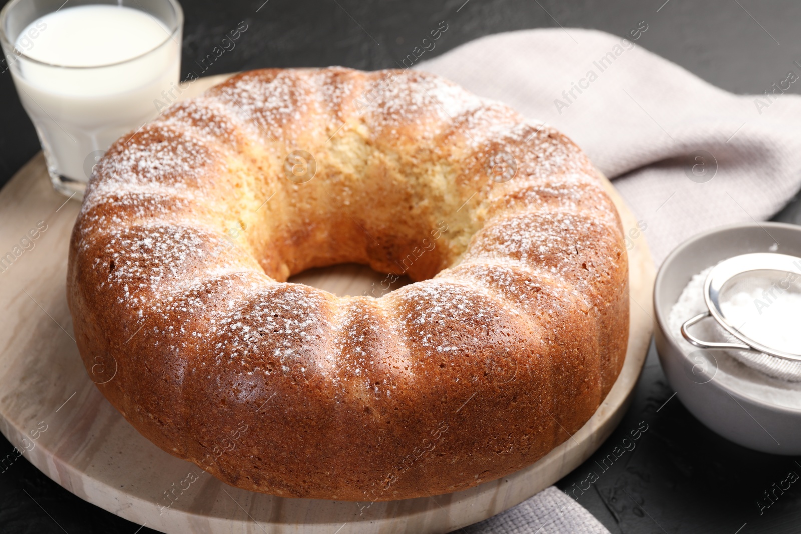 Photo of Freshly baked sponge cake with powdered sugar and milk on black table, closeup