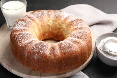 Freshly baked sponge cake with powdered sugar and milk on black table, closeup