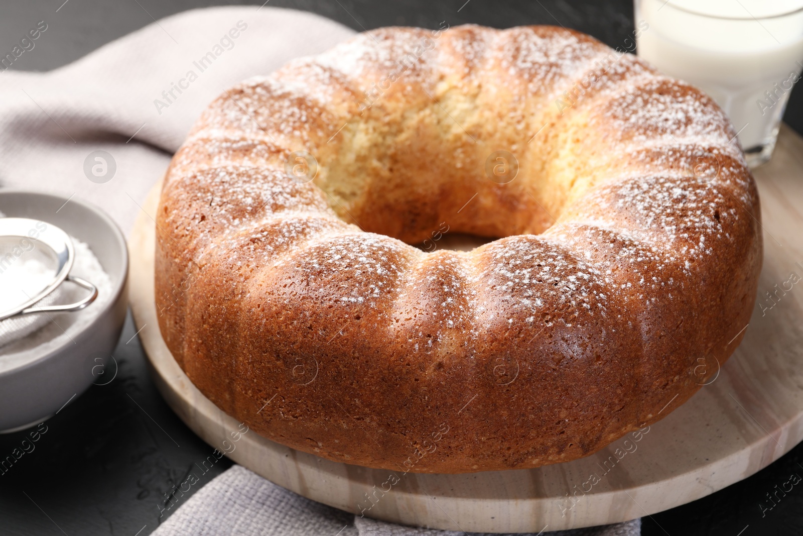 Photo of Freshly baked sponge cake with powdered sugar and milk on black table, closeup