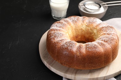 Photo of Freshly baked sponge cake with powdered sugar and milk on black table, closeup