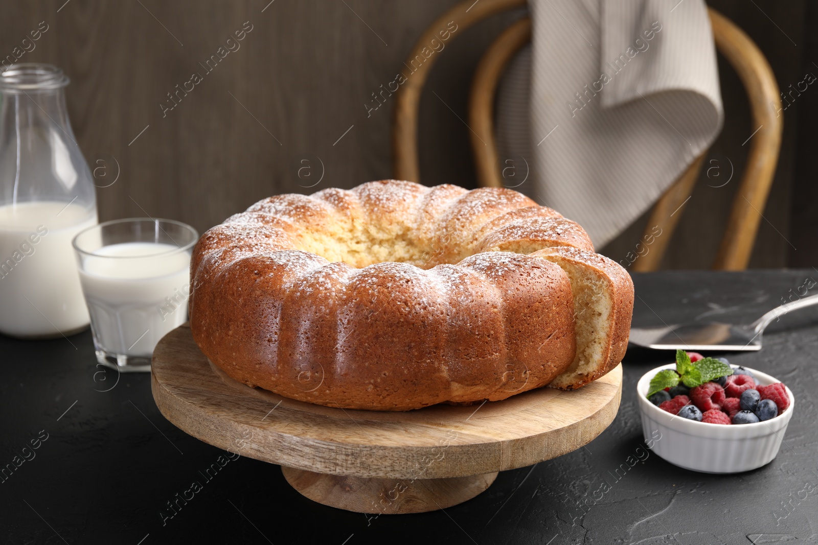 Photo of Freshly baked sponge cake, berries, milk and server on black table, closeup