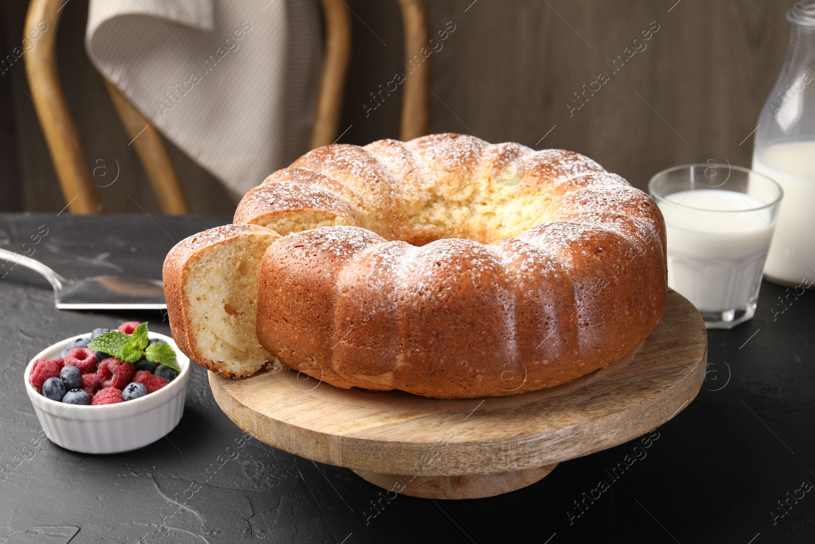 Photo of Freshly baked sponge cake, berries, milk and server on black table, closeup