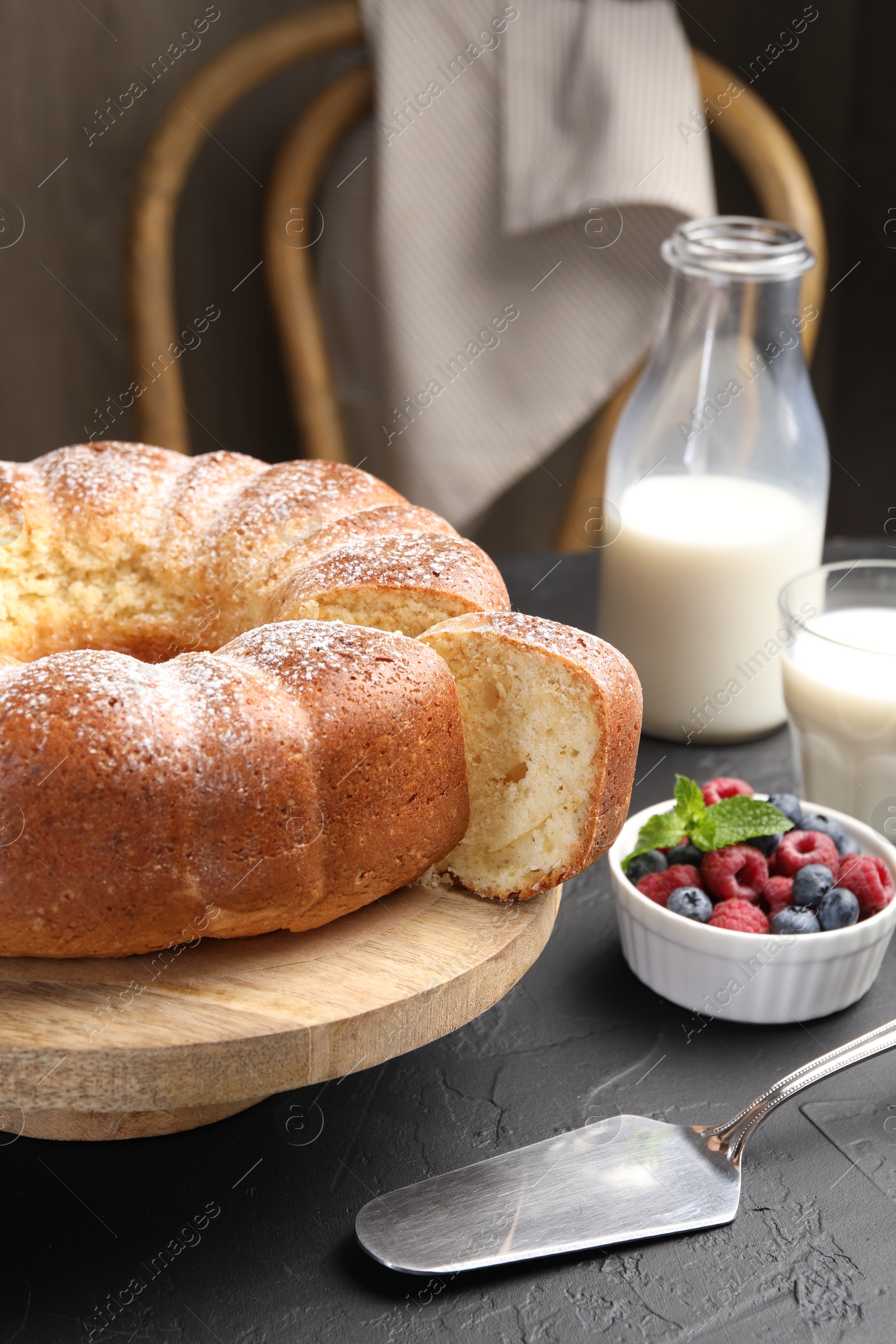 Photo of Freshly baked sponge cake, berries, milk and server on black table, closeup