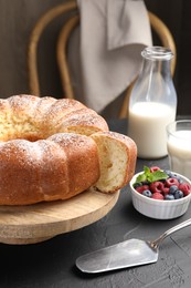 Photo of Freshly baked sponge cake, berries, milk and server on black table, closeup