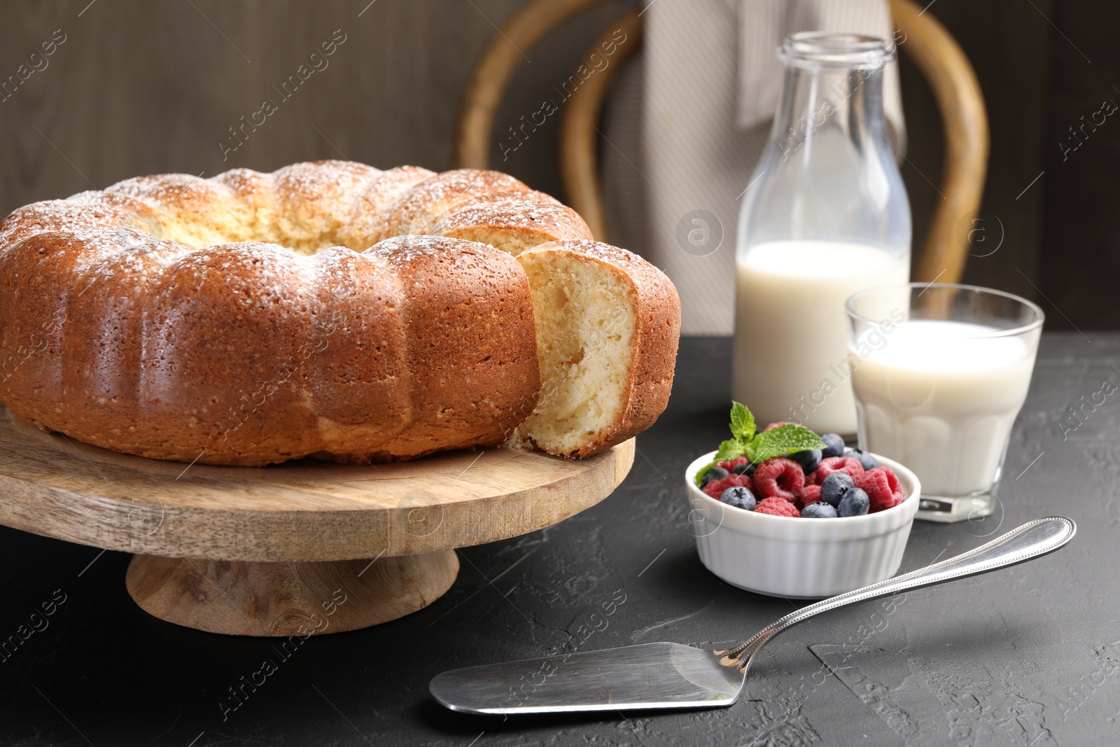 Photo of Freshly baked sponge cake, berries, milk and server on black table