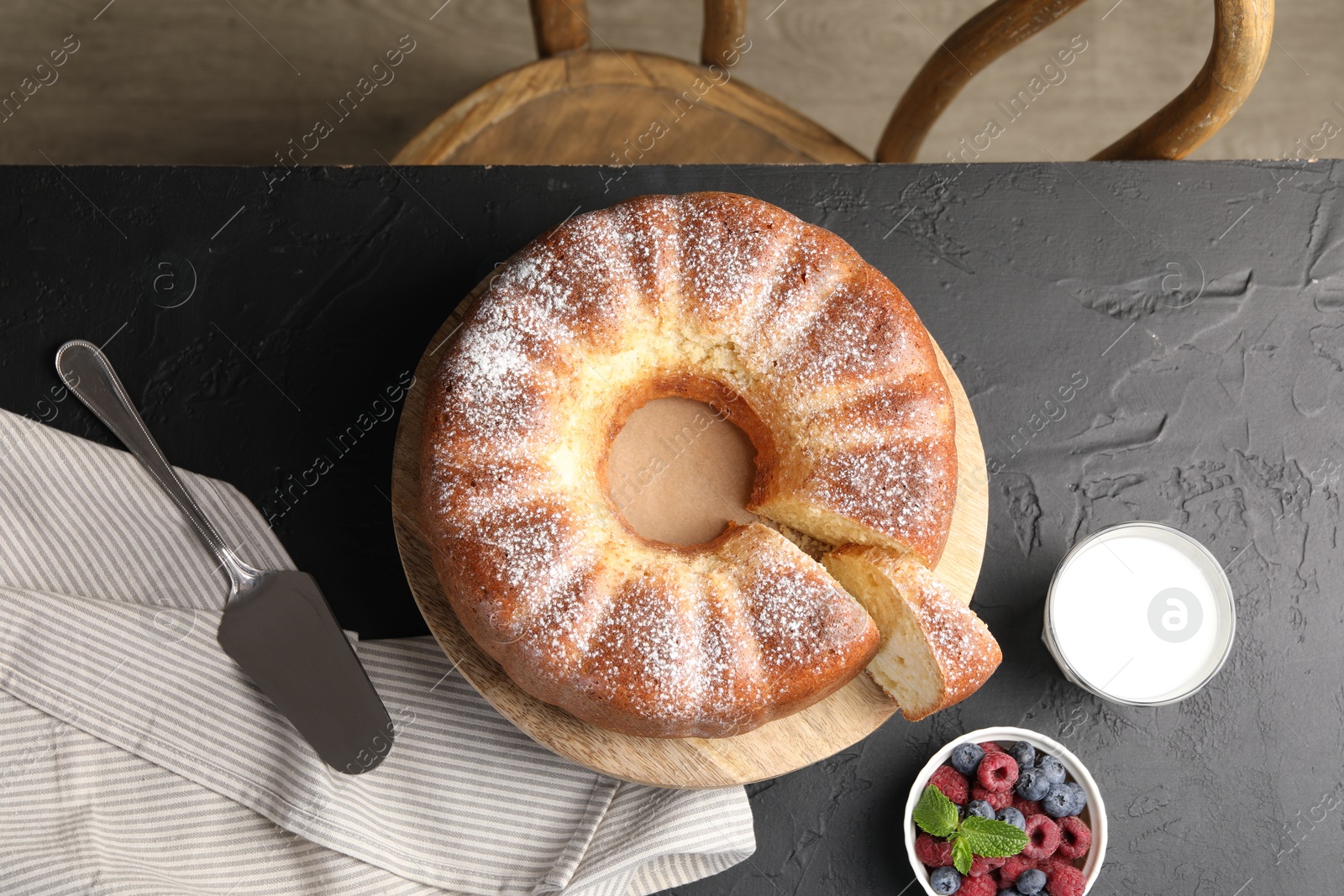 Photo of Freshly baked sponge cake, berries, milk and server on black table, top view