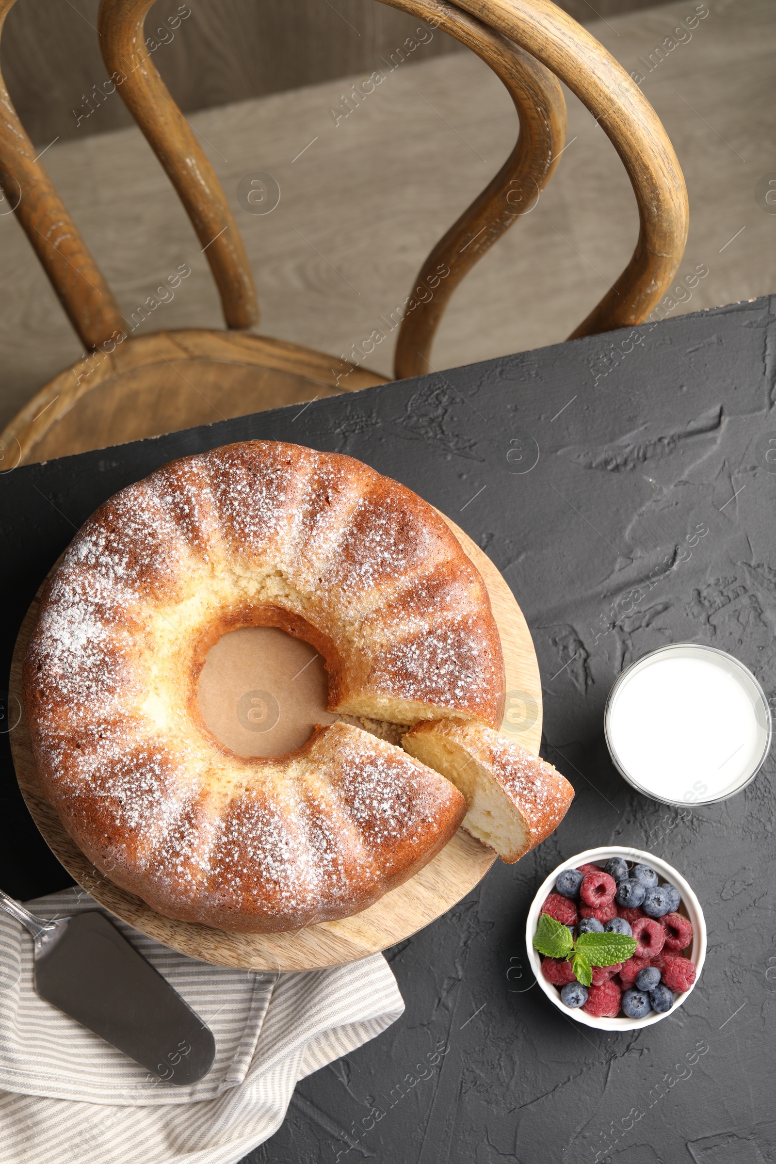 Photo of Freshly baked sponge cake, berries, milk and server on black table, top view