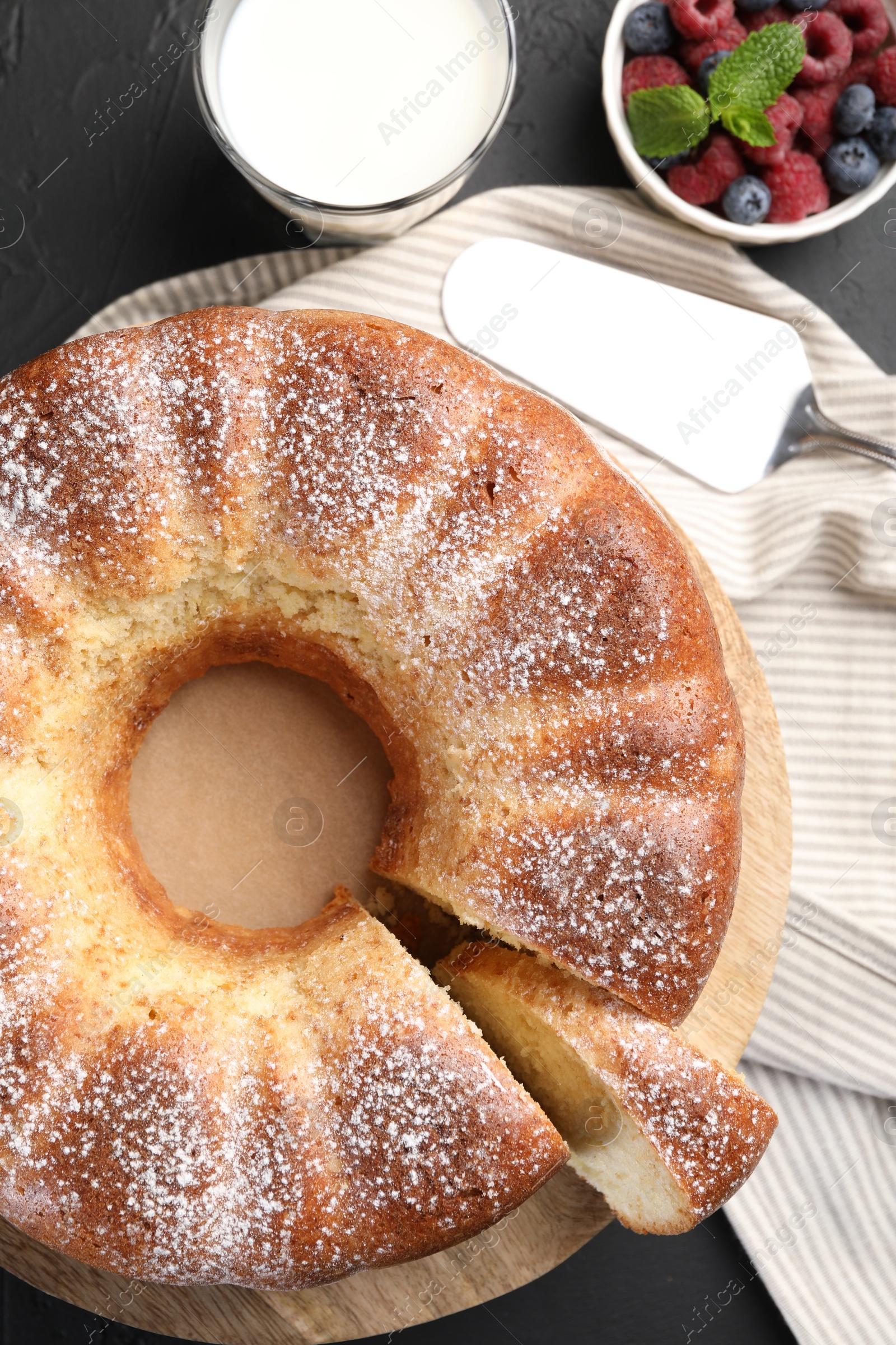 Photo of Freshly baked sponge cake, berries, milk and server on black table, top view