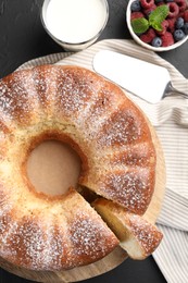 Freshly baked sponge cake, berries, milk and server on black table, top view