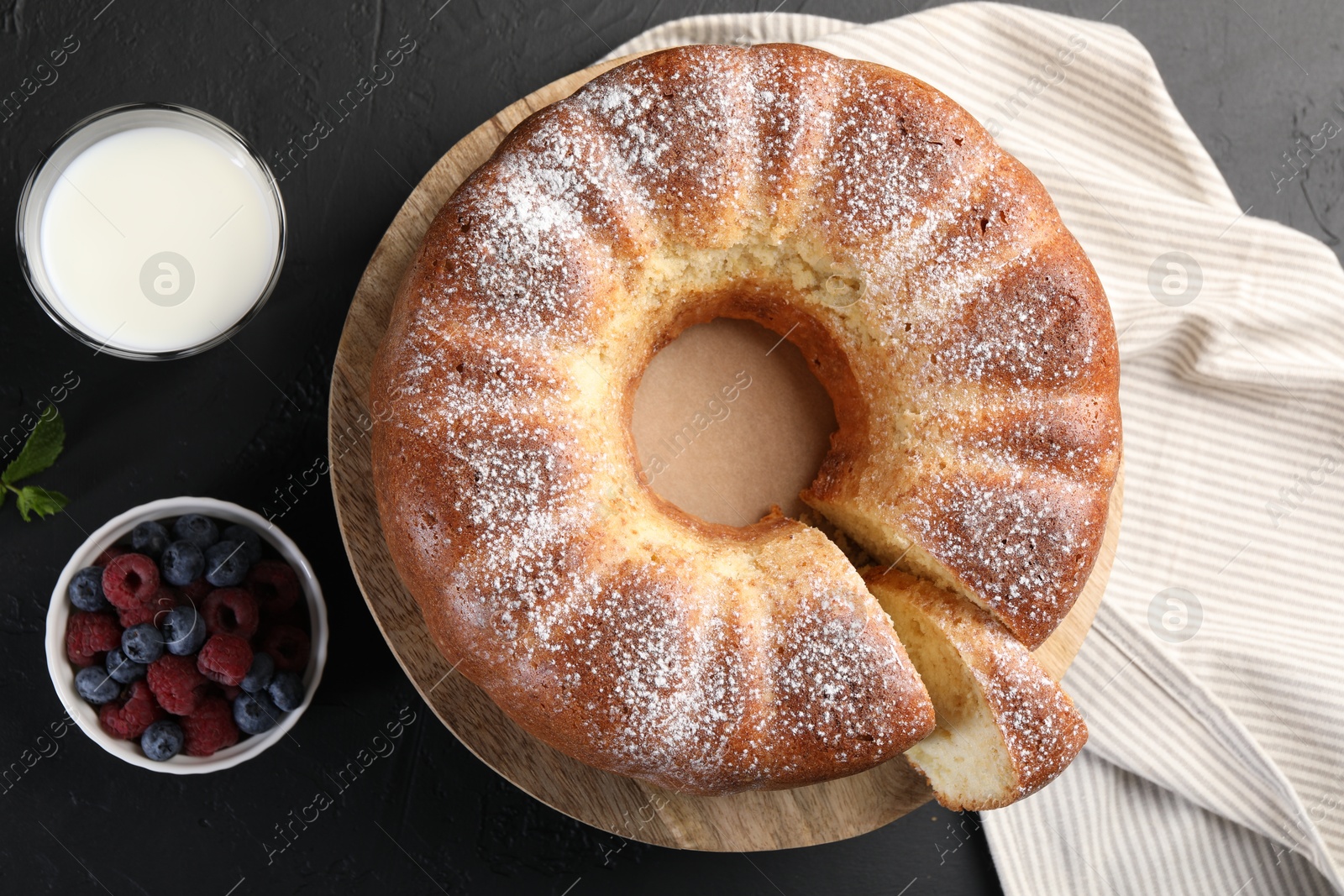 Photo of Freshly baked sponge cake, berries and milk on black table, top view