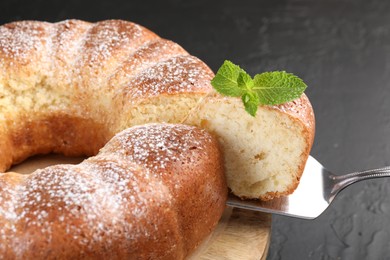 Taking piece of freshly baked sponge cake at black table, closeup