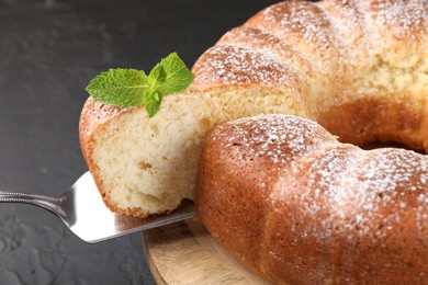 Taking piece of freshly baked sponge cake at black table, closeup