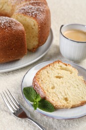 Piece of freshly baked sponge cake, mint and coffee on white textured table, closeup