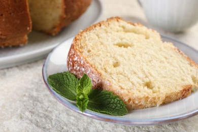 Photo of Piece of freshly baked sponge cake and mint on white textured table, closeup