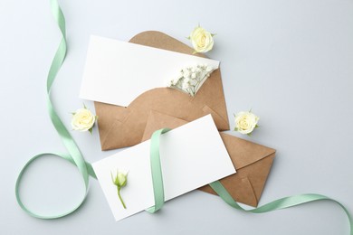 Photo of Blank cards, envelopes, flowers and ribbon on light grey table, flat lay