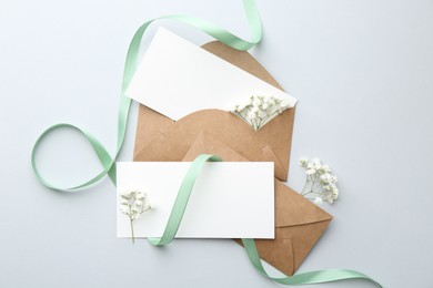 Blank cards, envelopes, flowers and ribbon on light grey table, flat lay