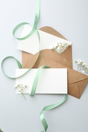 Photo of Blank cards, envelopes, flowers and ribbon on light grey table, flat lay