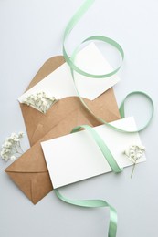 Blank cards, envelopes, flowers and ribbon on light grey table, flat lay