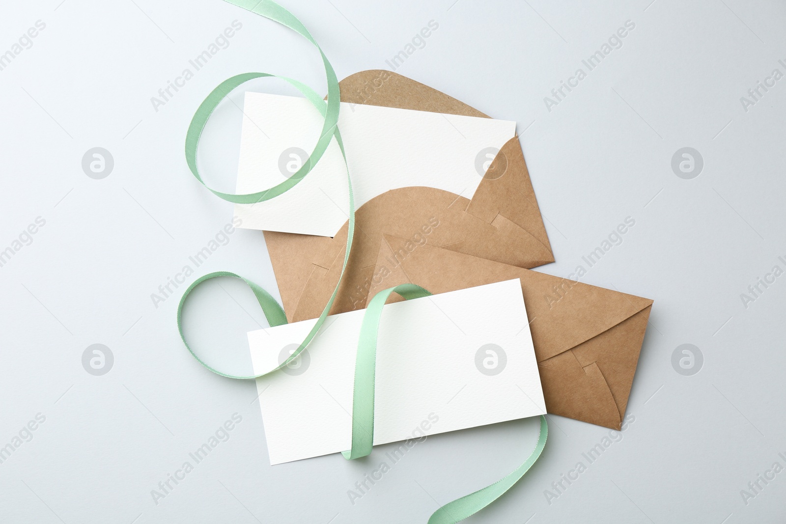 Photo of Blank cards, envelopes and ribbon on light grey table, flat lay