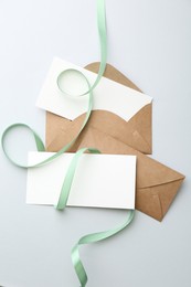 Photo of Blank cards, envelopes and ribbon on light grey table, flat lay